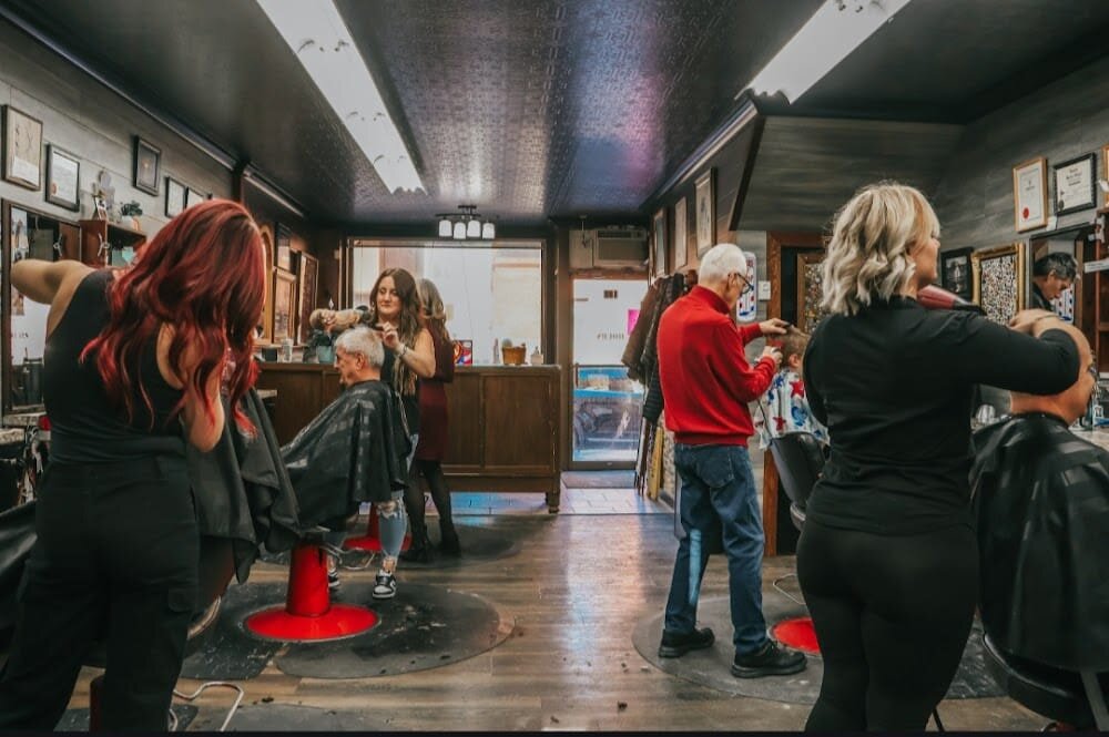 Inside the shop on a busy day, barbers working at their chairs under the tin ceiling