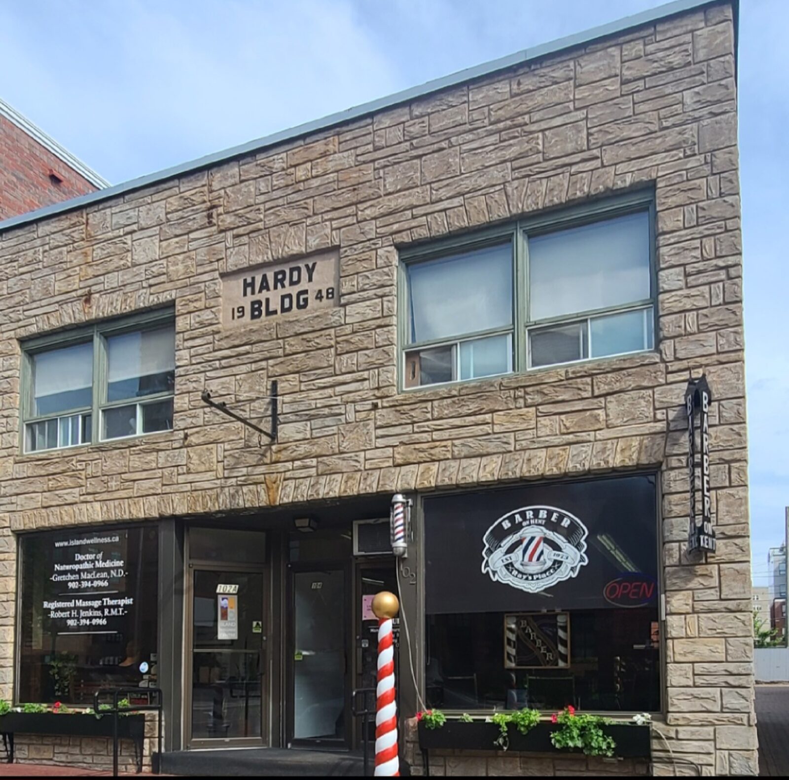 The stone front of the Hardy Building at 102 Kent Street, with the Ray's Place barber pole and window sign
